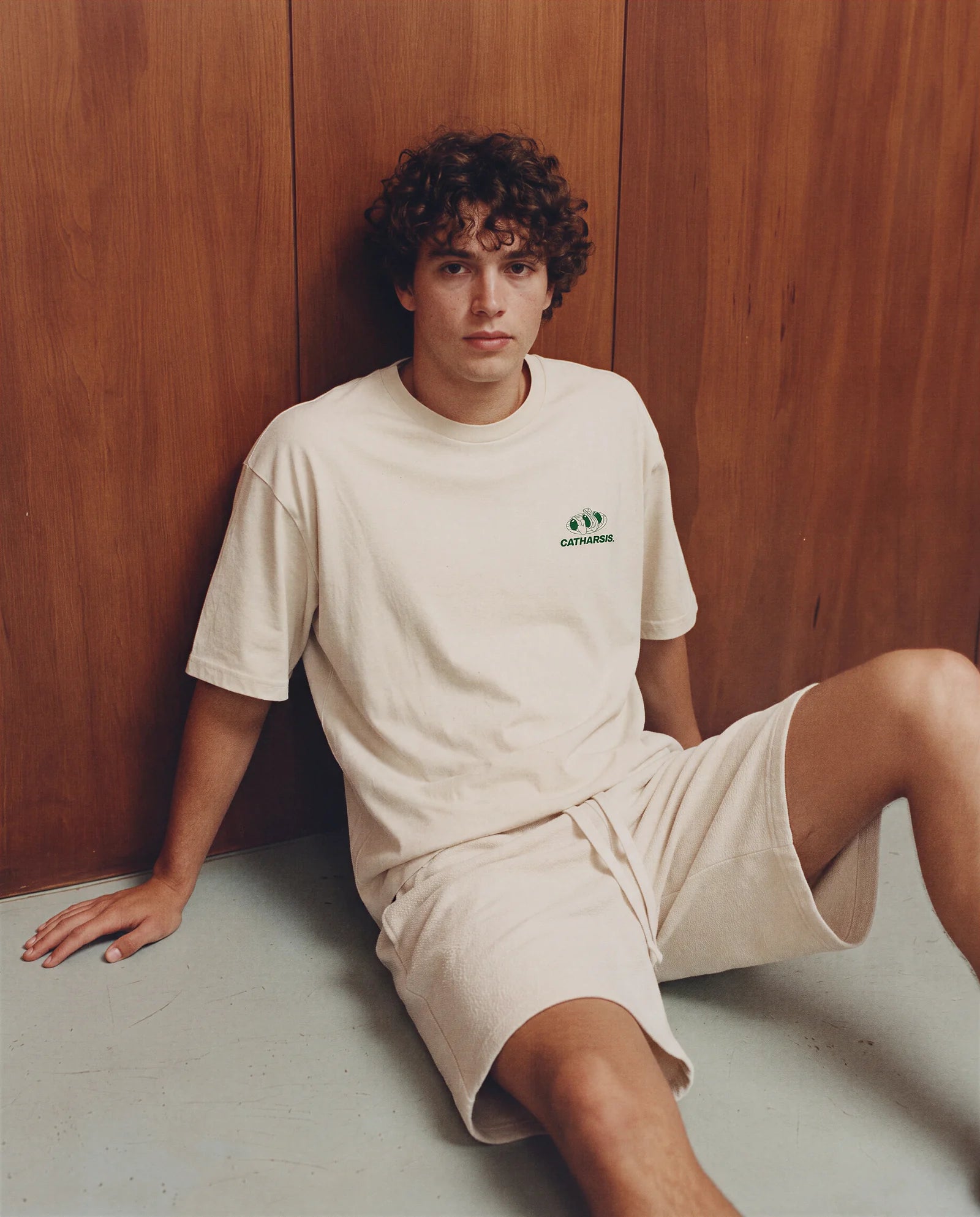 Model sitting on the floor in the relaxed Gildas T-shirt and cream shorts. Image created or edited with AI.