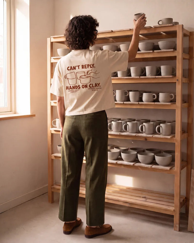 The woman, seen from behind, puts a mug on a wooden drying rack, with the large Can't Reply print on her back. Image created or edited with AI.