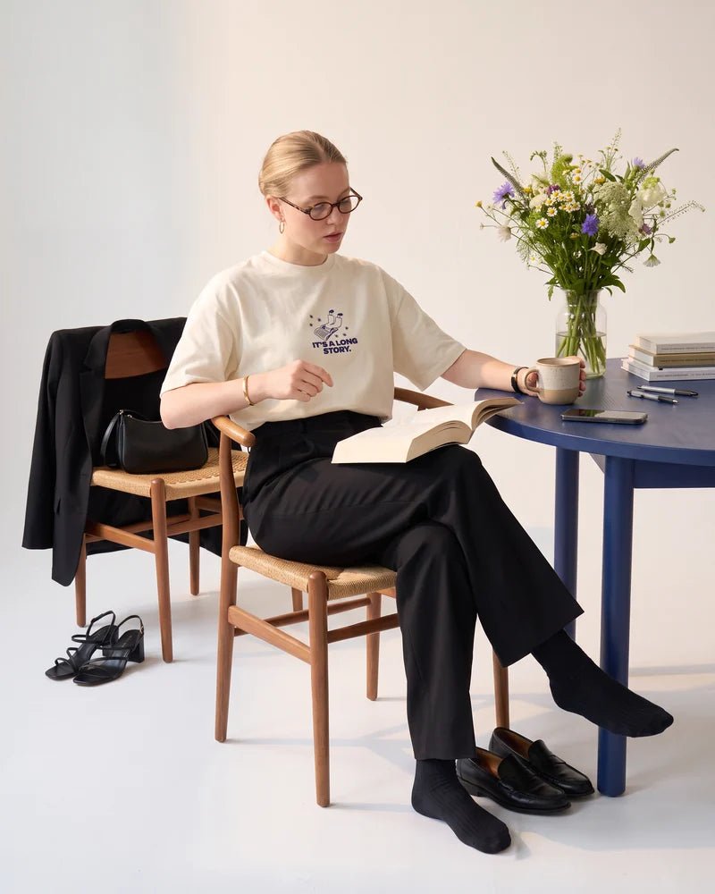 Woman sitting at the blue table with her morning coffee and the book just started, wearing the cropped T-shirt Sorry, I can't make it. It's a long story. AI-generated image.