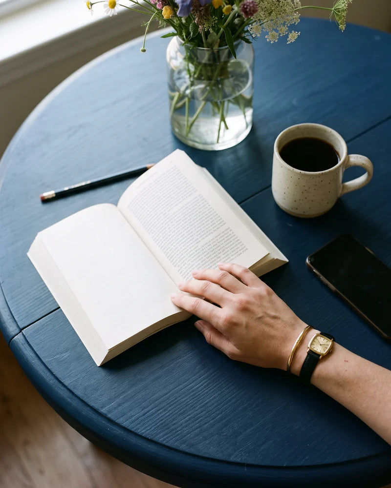 Detail: the table in the morning: a coffee, the phone face down and the book on page one. AI-generated image.