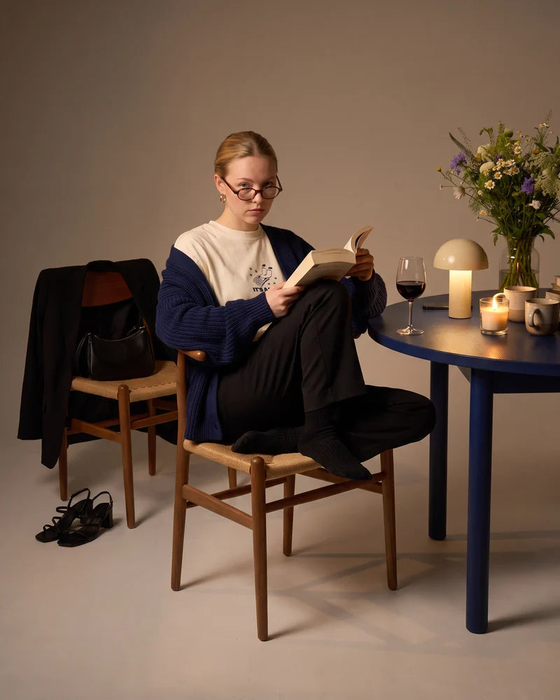 Woman at night, curled up on the chair in a cardigan with the book almost finished, wearing the cropped T-shirt Sorry, I can't make it. It's a long story. AI-generated image.