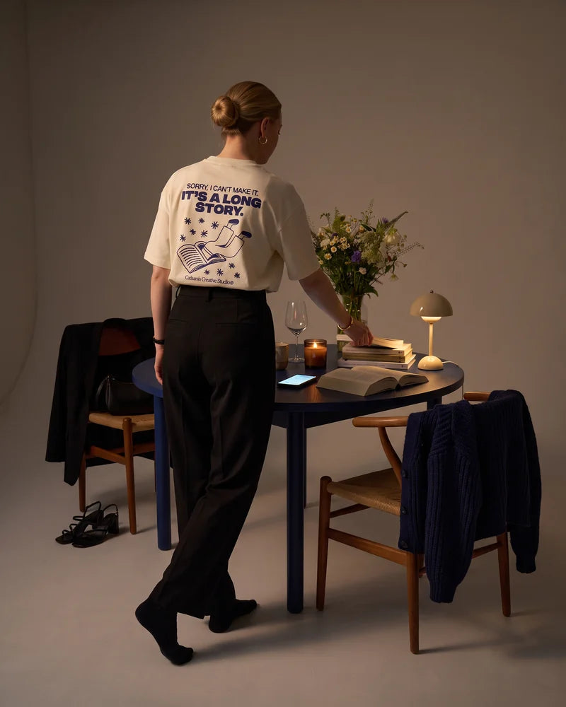 Woman seen from behind, reaching for the next book after midnight, wearing the cropped T-shirt Sorry, I can't make it. It's a long story. AI-generated image.