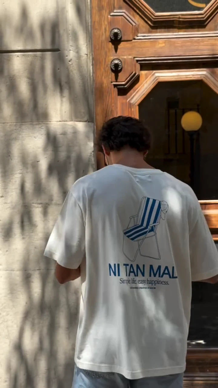 The cream Ni Tan Mal T-shirt with a blue beach-chair graphic by a wooden door.