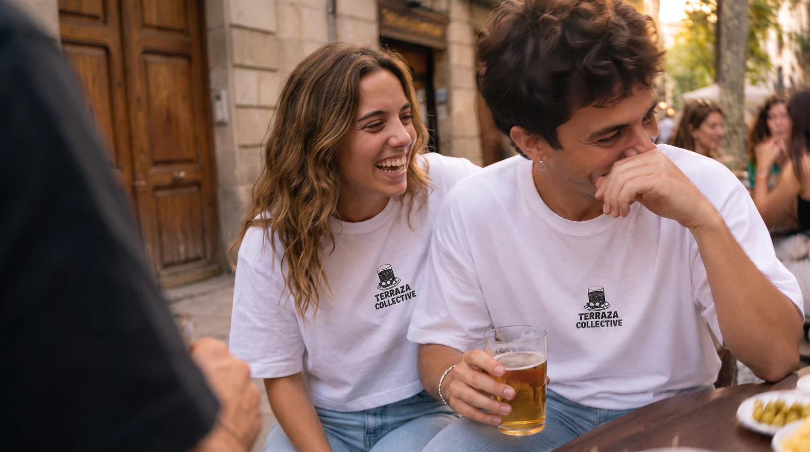 Two friends laughing on a terrace in the Terraza Collective relaxed and cropped T-shirts. Image created or edited with AI.